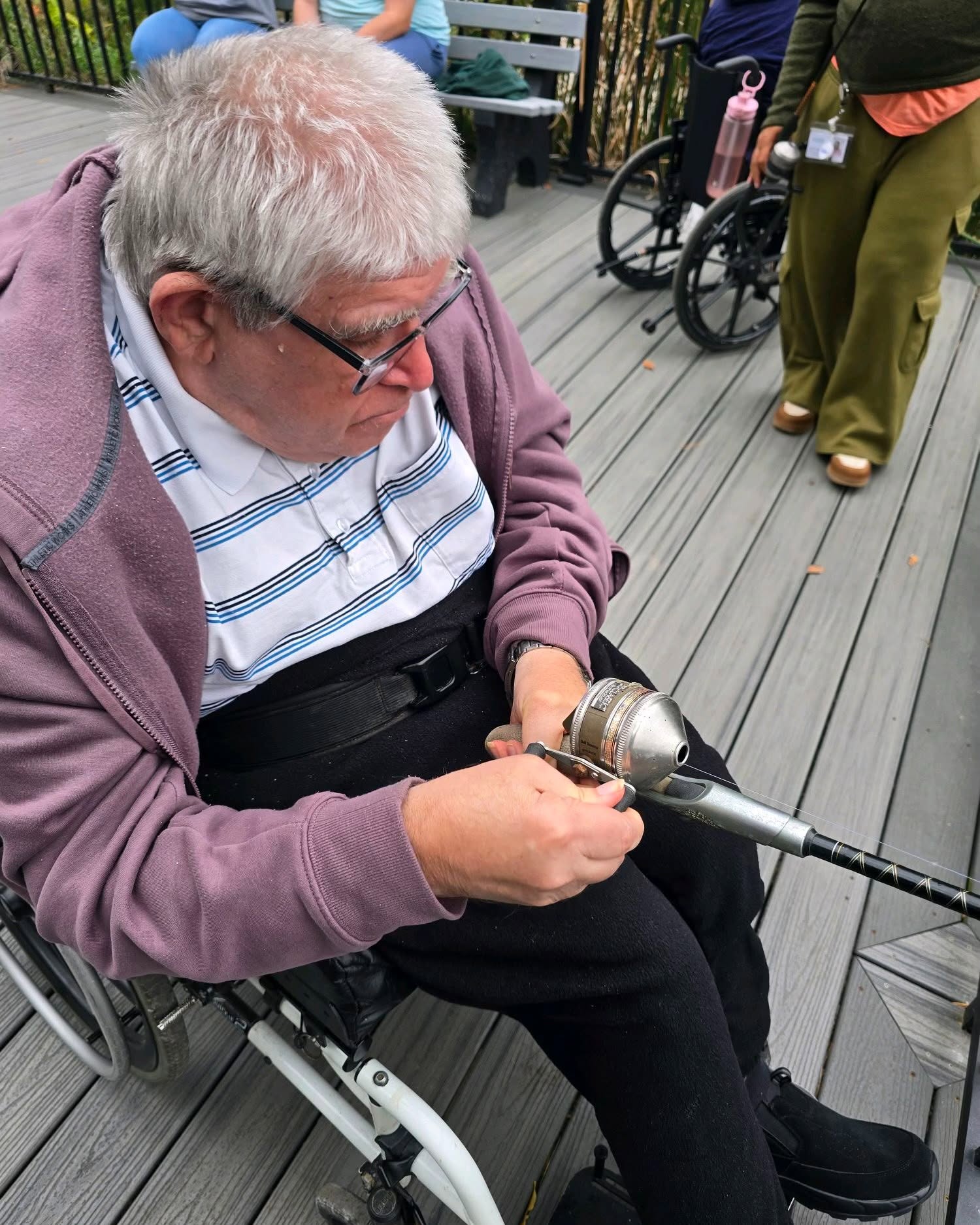 Man in a wheelchair holding a fishing rod on a boardwalk